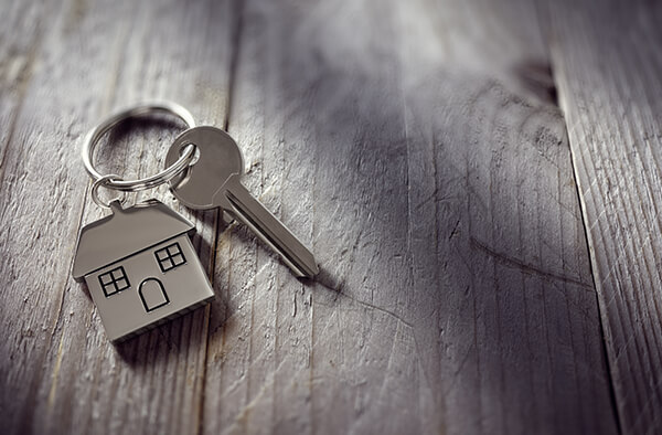 Image of a key chain in the shape of a house with a key on the chain, sitting on top of a gray table