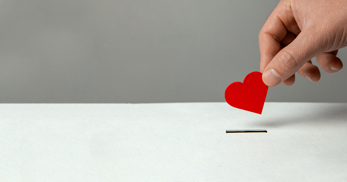 Man’s hand places heart in the donation slot.