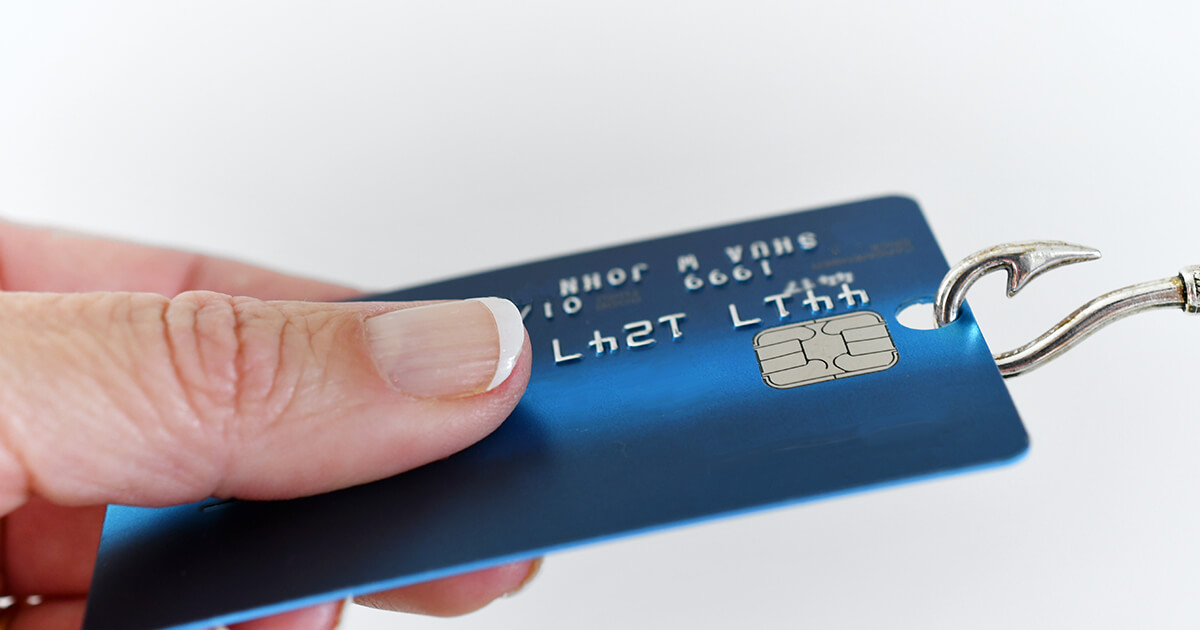 Hand holding a credit card that is being pulled away from them with a fish hook. Meant to represent the term 'phishing'.